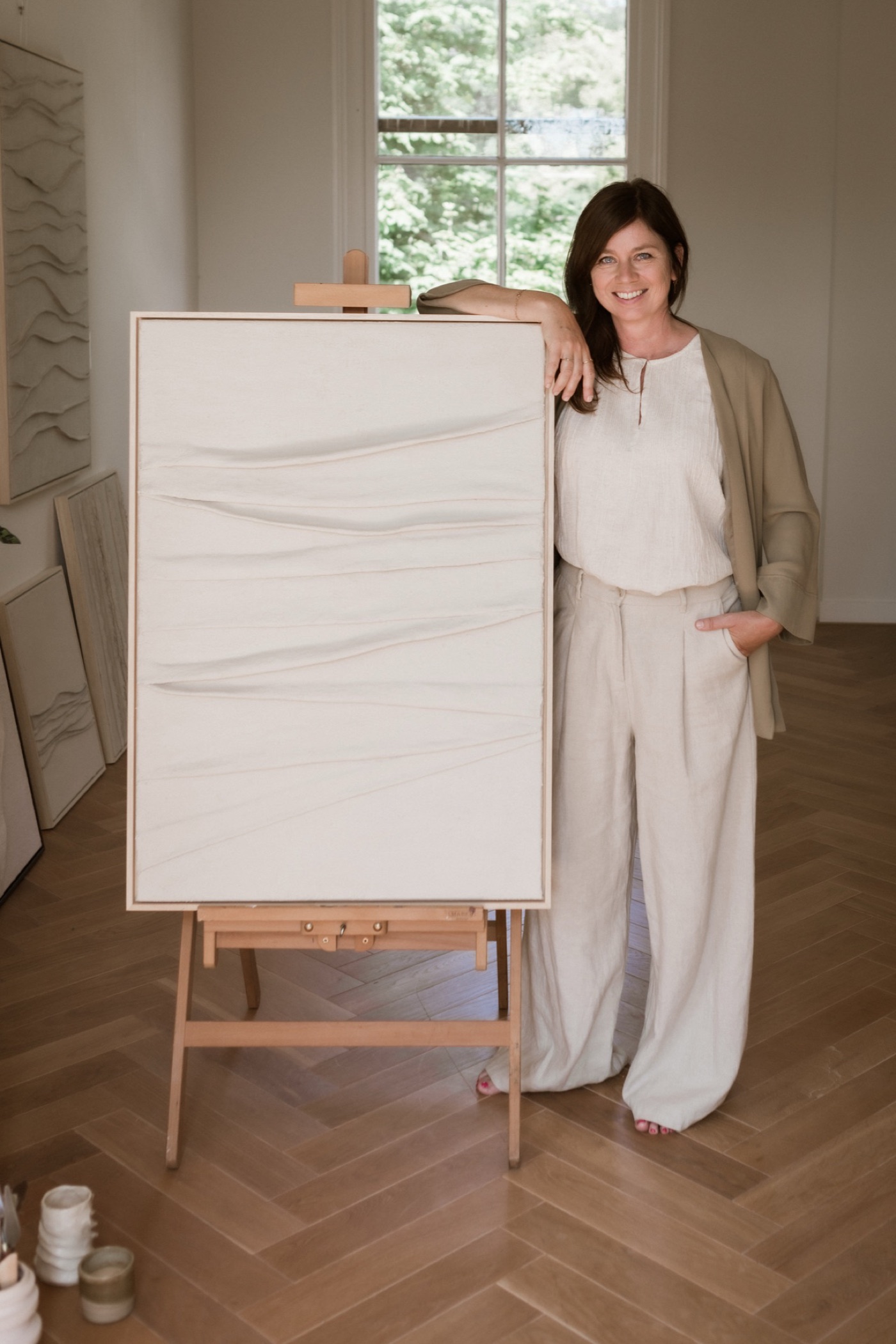 Ilse naast haar werk op een ezel — linnen outfit, atelier